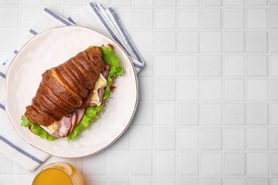 Tasty croissant with brie cheese, ham and bacon on white tiled table, flat lay. Space for text