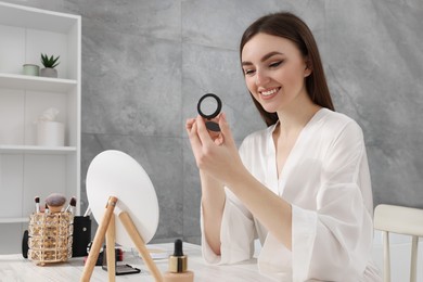 Photo of Beautiful young woman with blusher at dressing table indoors
