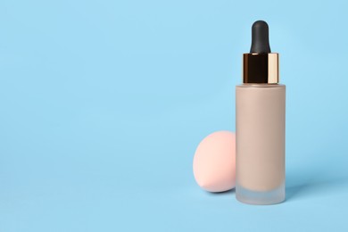 Photo of Bottle of skin foundation and sponge on light blue background, space for text. Makeup product