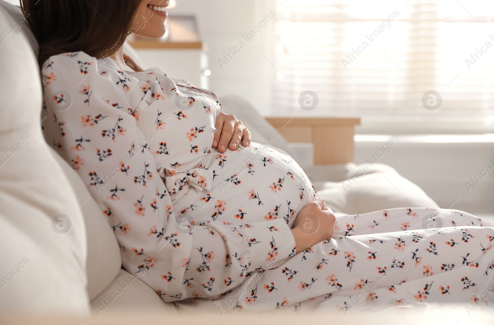 Photo of Young pregnant woman sitting on sofa at home, closeup