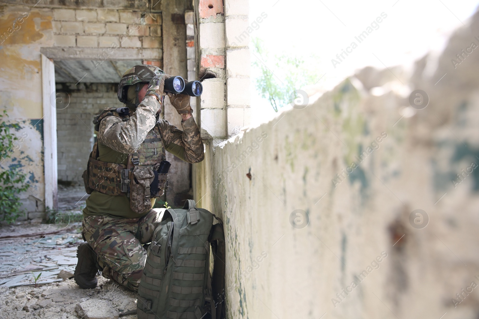 Photo of Military mission. Soldier in uniform with binoculars inside abandoned building, space for text