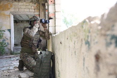 Military mission. Soldier in uniform with binoculars inside abandoned building, space for text