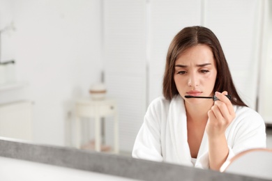 Photo of Young woman holding mascara brush with fallen eyelashes indoors