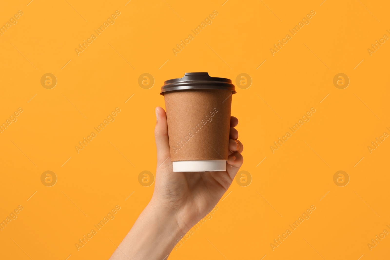 Photo of Woman holding takeaway paper coffee cup on orange background, closeup