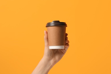 Woman holding takeaway paper coffee cup on orange background, closeup