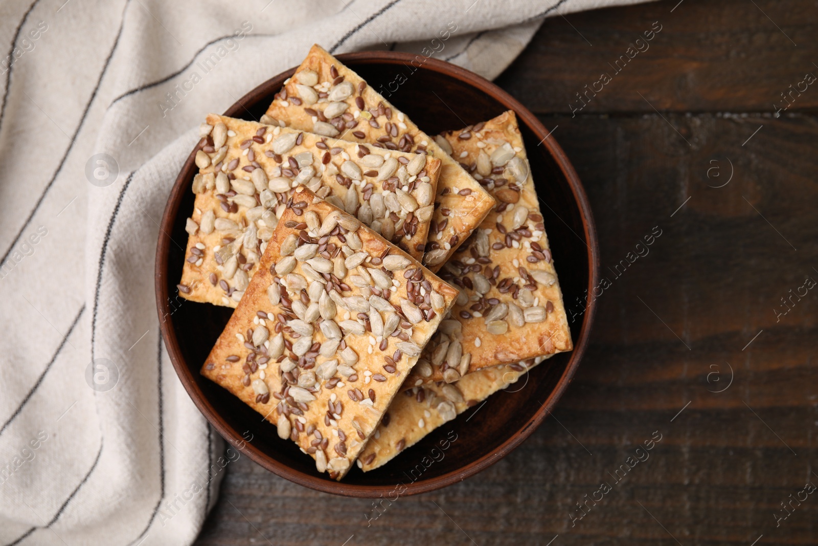 Photo of Cereal crackers with flax, sunflower and sesame seeds in bowl on wooden table, top view
