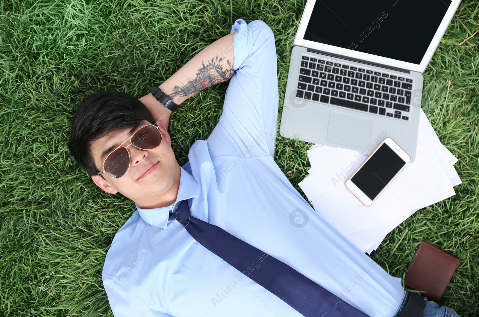 Photo of Young man lying on green lawn in park, top view. Joy in moment