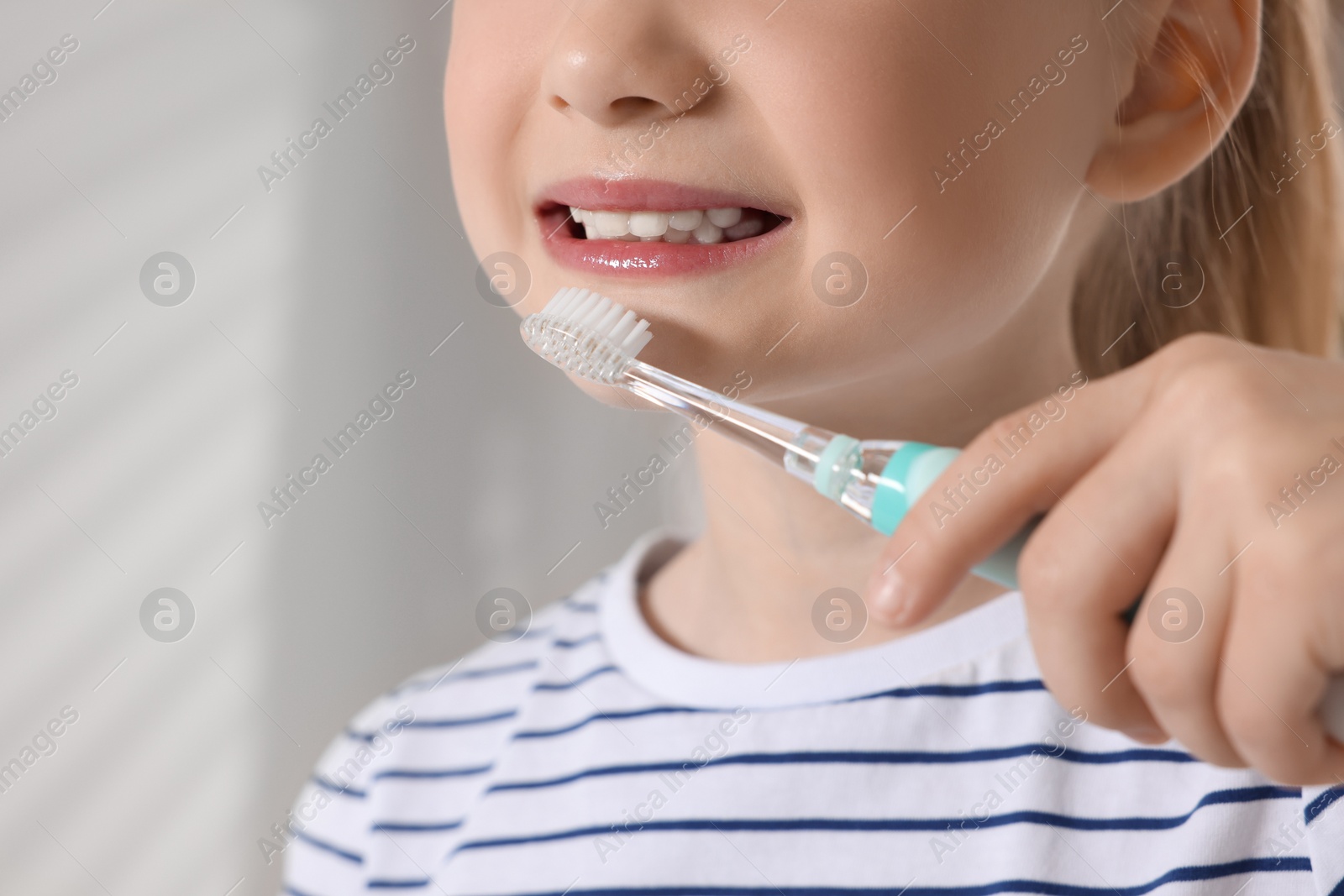 Photo of Little girl brushing her teeth with electric toothbrush indoors, closeup. Space for text