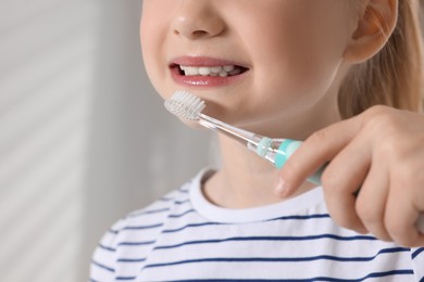 Photo of Little girl brushing her teeth with electric toothbrush indoors, closeup. Space for text