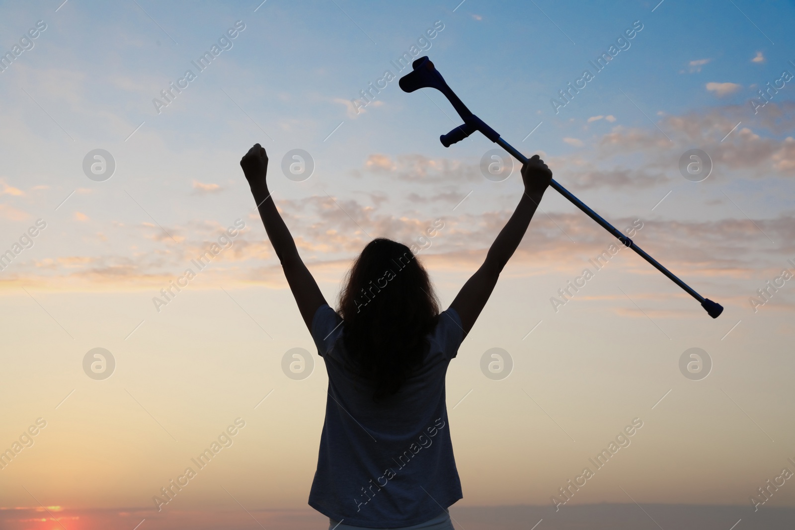 Photo of Woman holding elbow crutch outdoors at sunrise, back view. Healing miracle