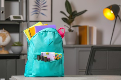 Photo of Turquoise backpack with different school stationery on table indoors, space for text
