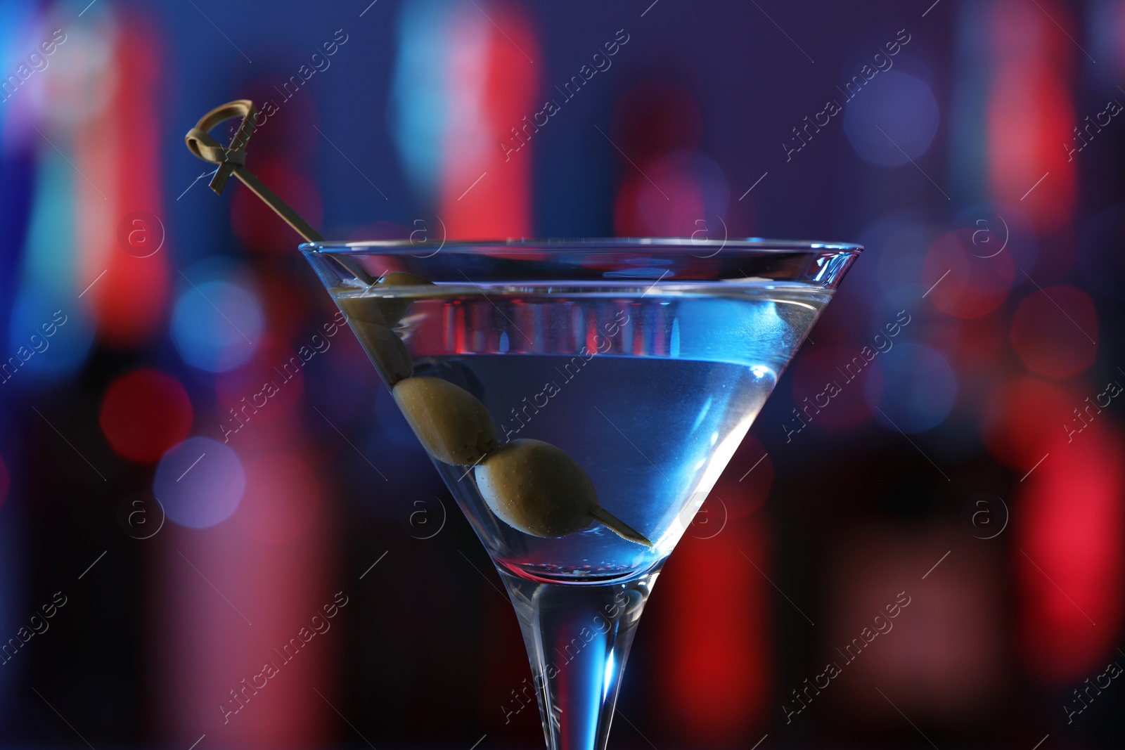 Photo of Martini glass with cocktail and olives in bar, closeup