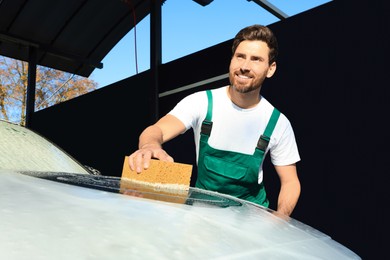 Photo of Worker washing auto with sponge at outdoor car wash