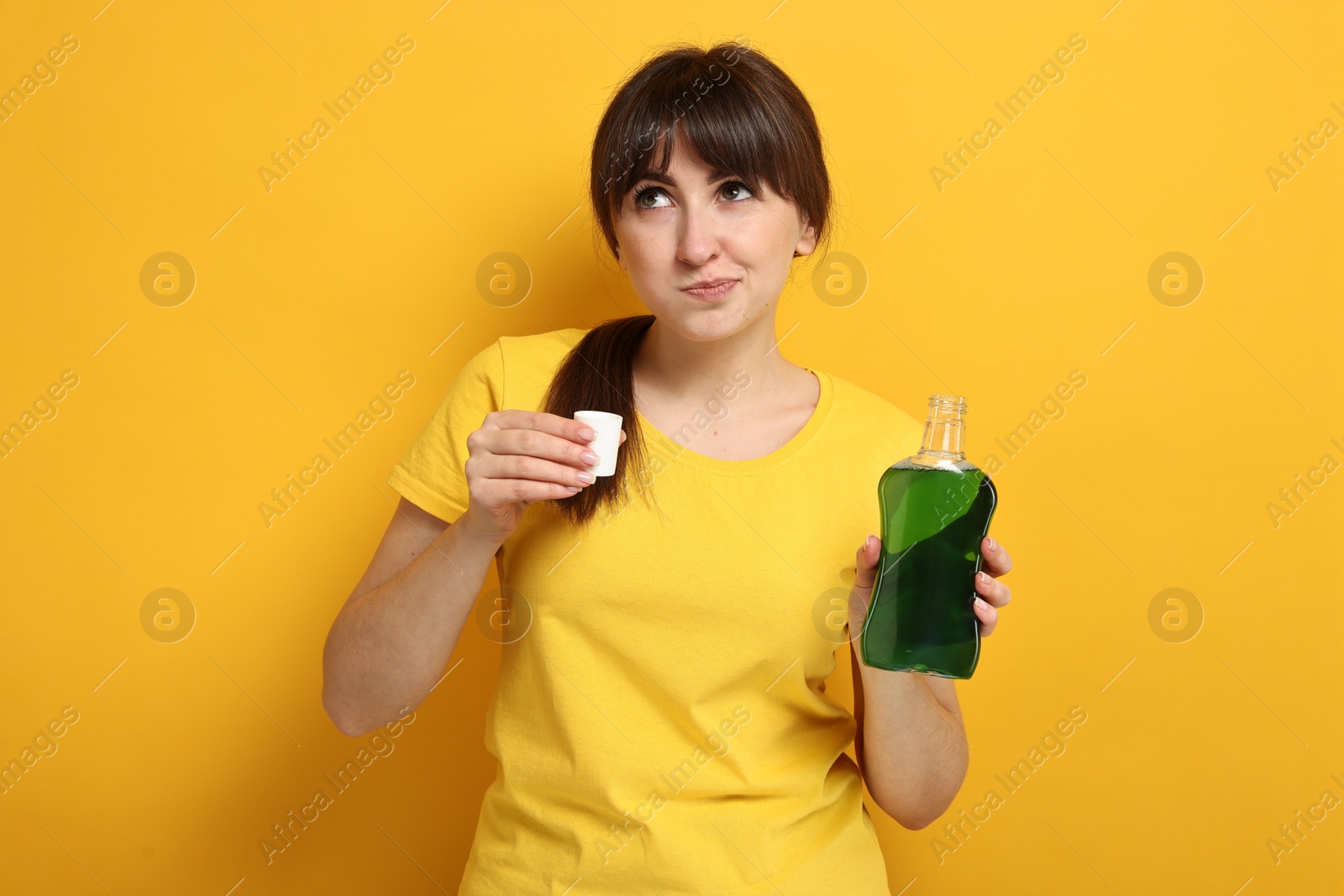 Photo of Young woman using mouthwash on yellow background