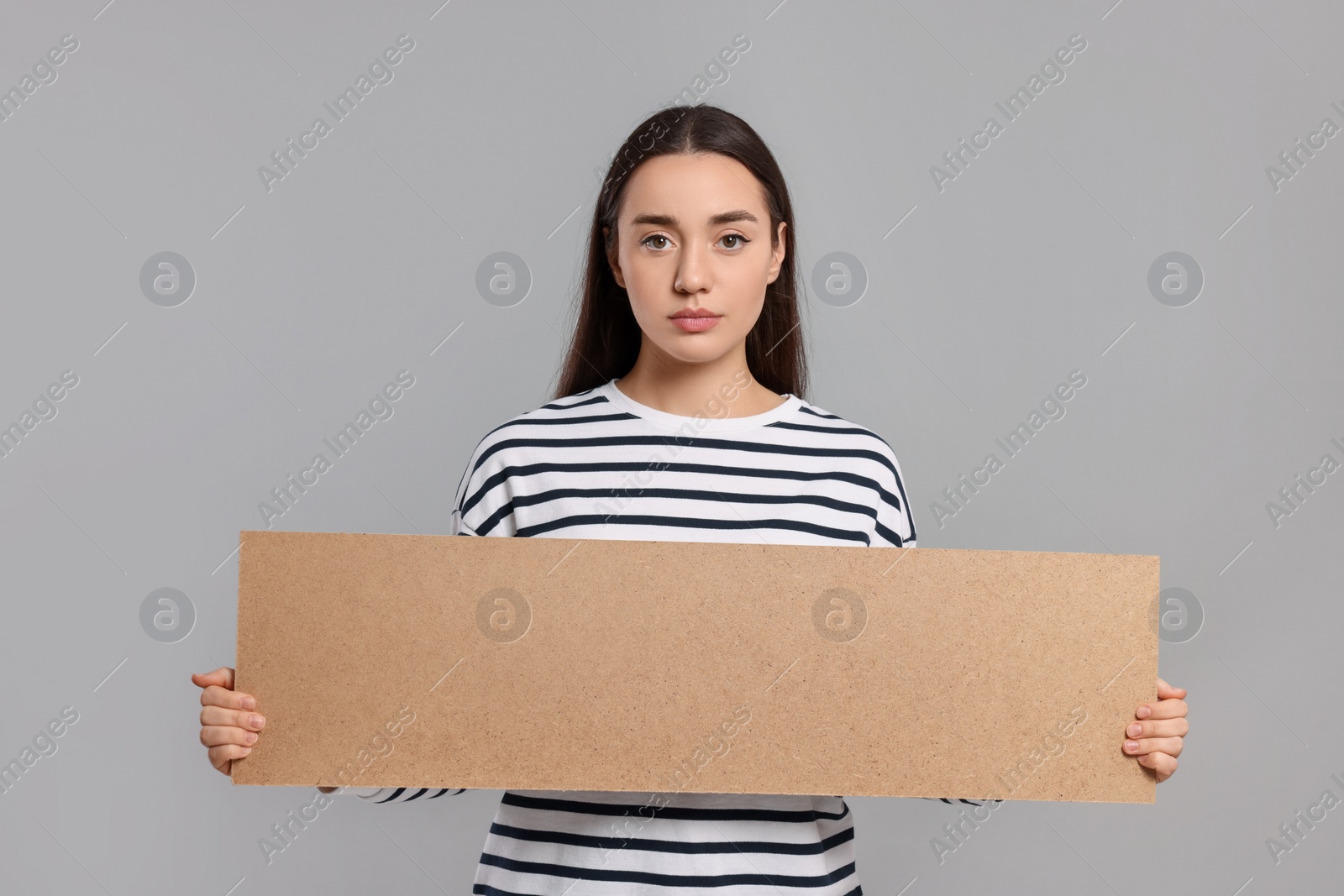 Photo of Young woman holding blank cardboard banner on light grey background, space for text