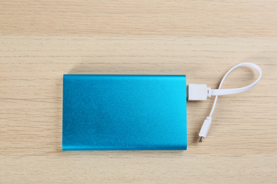 Photo of Modern portable charger with cable on wooden background, top view