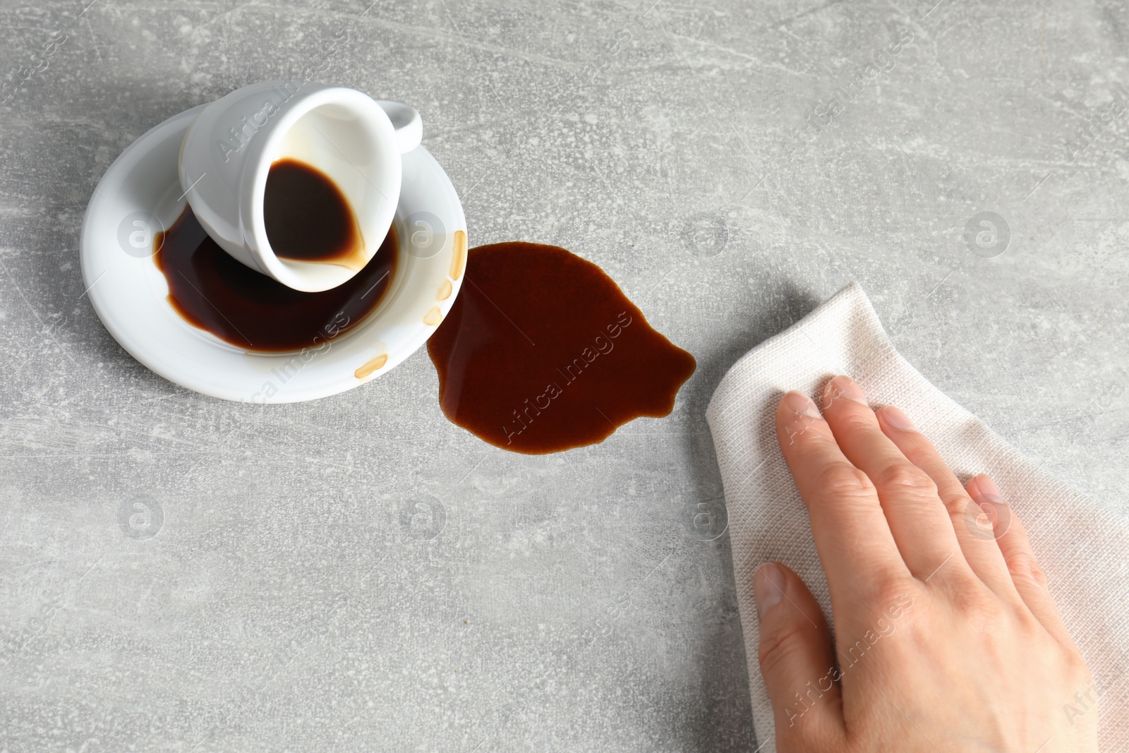 Photo of Woman wiping spilled coffee on grey table, closeup