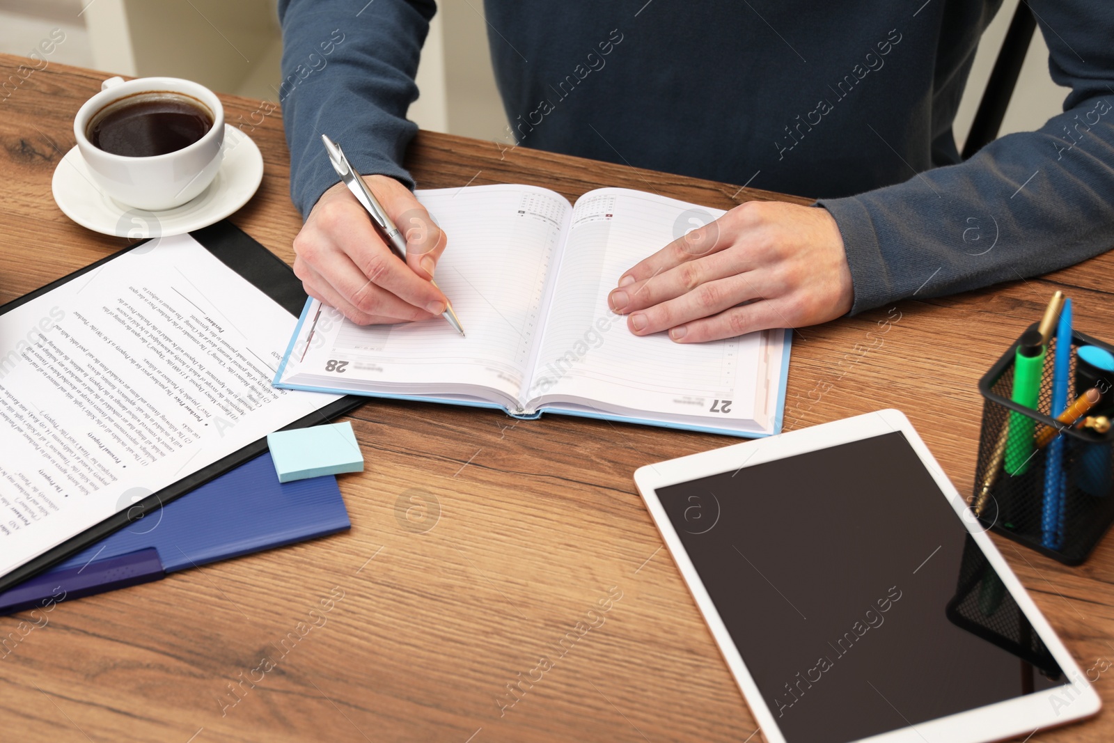 Photo of Man taking notes at wooden table, closeup