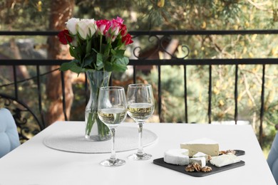 Beautiful roses, glasses of wine and snacks on white table at balcony