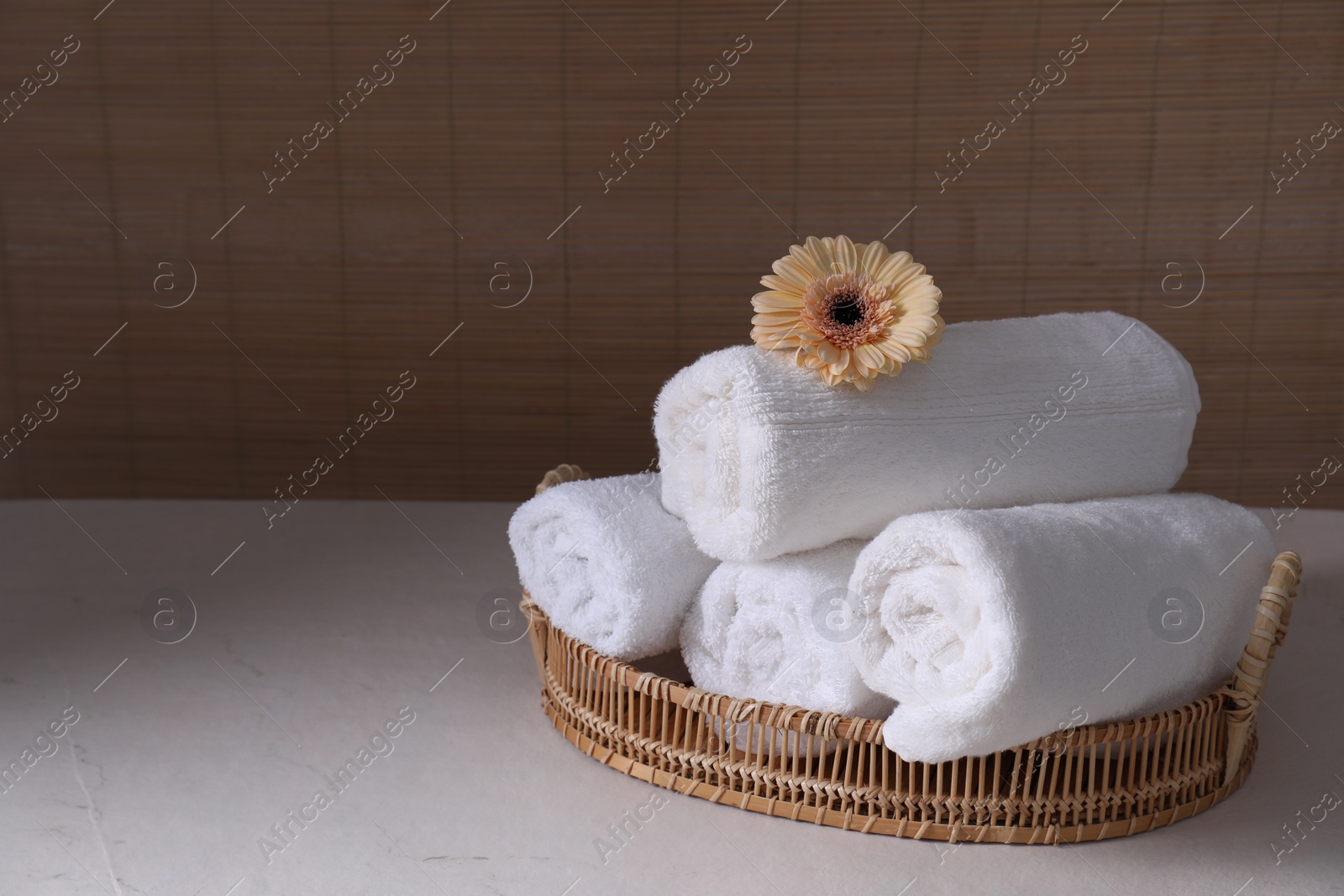 Photo of Rolled terry towels and flower on white table indoors, space for text