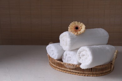 Photo of Rolled terry towels and flower on white table indoors, space for text