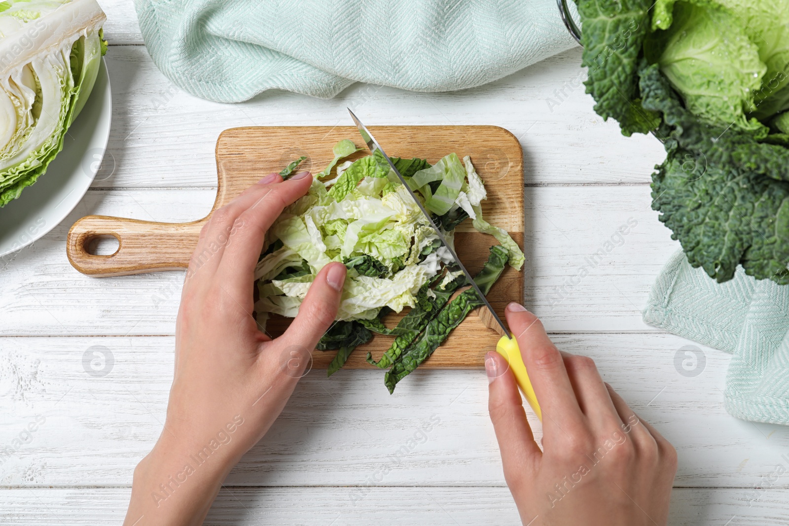 Photo of Woman cutting fresh green savoy cabbage at white wooden table, top view