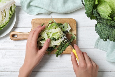 Woman cutting fresh green savoy cabbage at white wooden table, top view