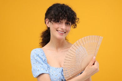Photo of Happy woman holding hand fan on orange background