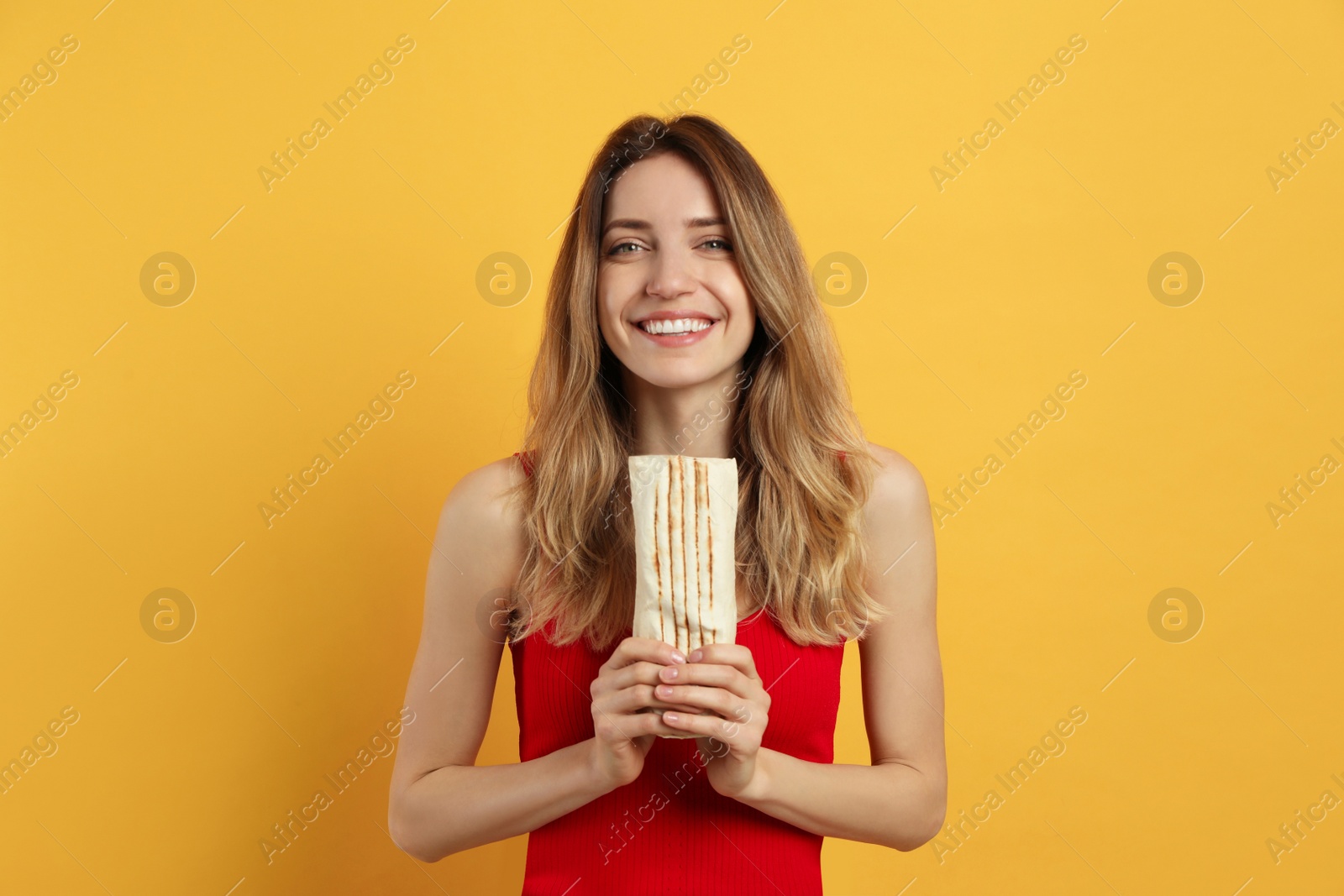 Photo of Young woman with delicious shawarma on yellow background