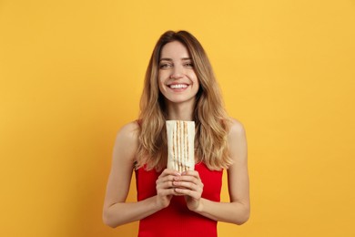 Photo of Young woman with delicious shawarma on yellow background