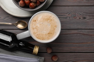 Photo of Mug of delicious coffee with hazelnut syrup on wooden table, flat lay. Space for text