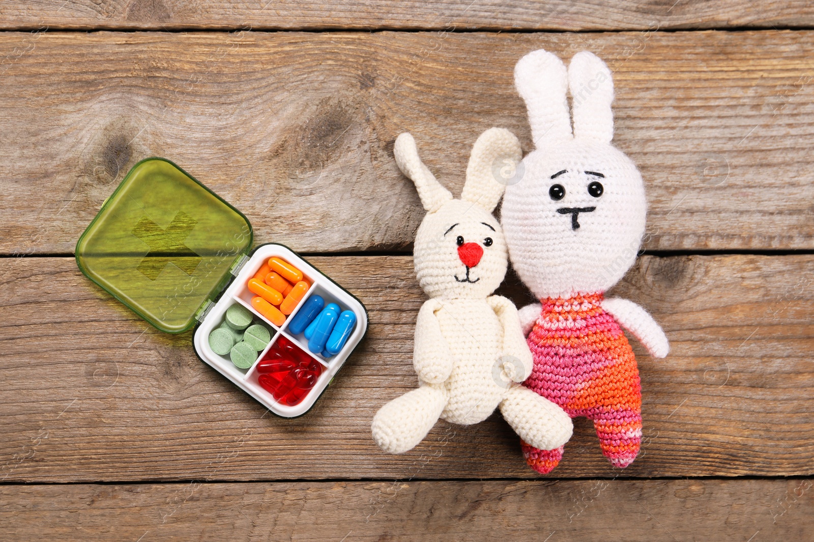 Photo of Toy bunnies and pills on wooden background, flat lay