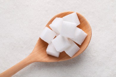 Different types of white sugar and spoon as background, top view