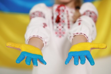 Photo of Little girl with painted hands near Ukrainian flag, closeup. Love Ukraine concept