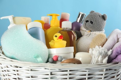 Photo of Wicker basket with baby cosmetic products and accessories on light blue background, closeup view