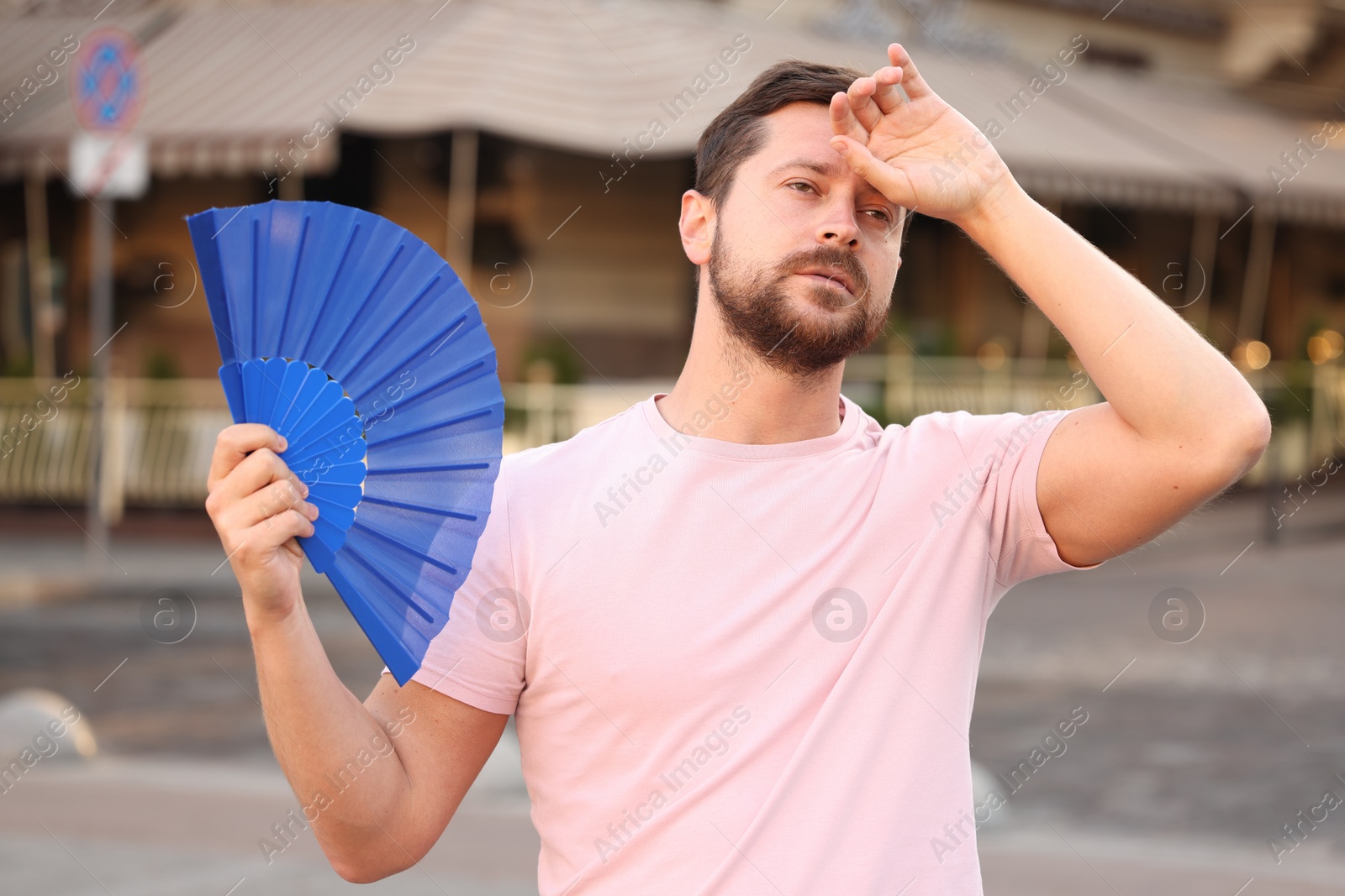 Photo of Man with hand fan suffering from heat outdoors