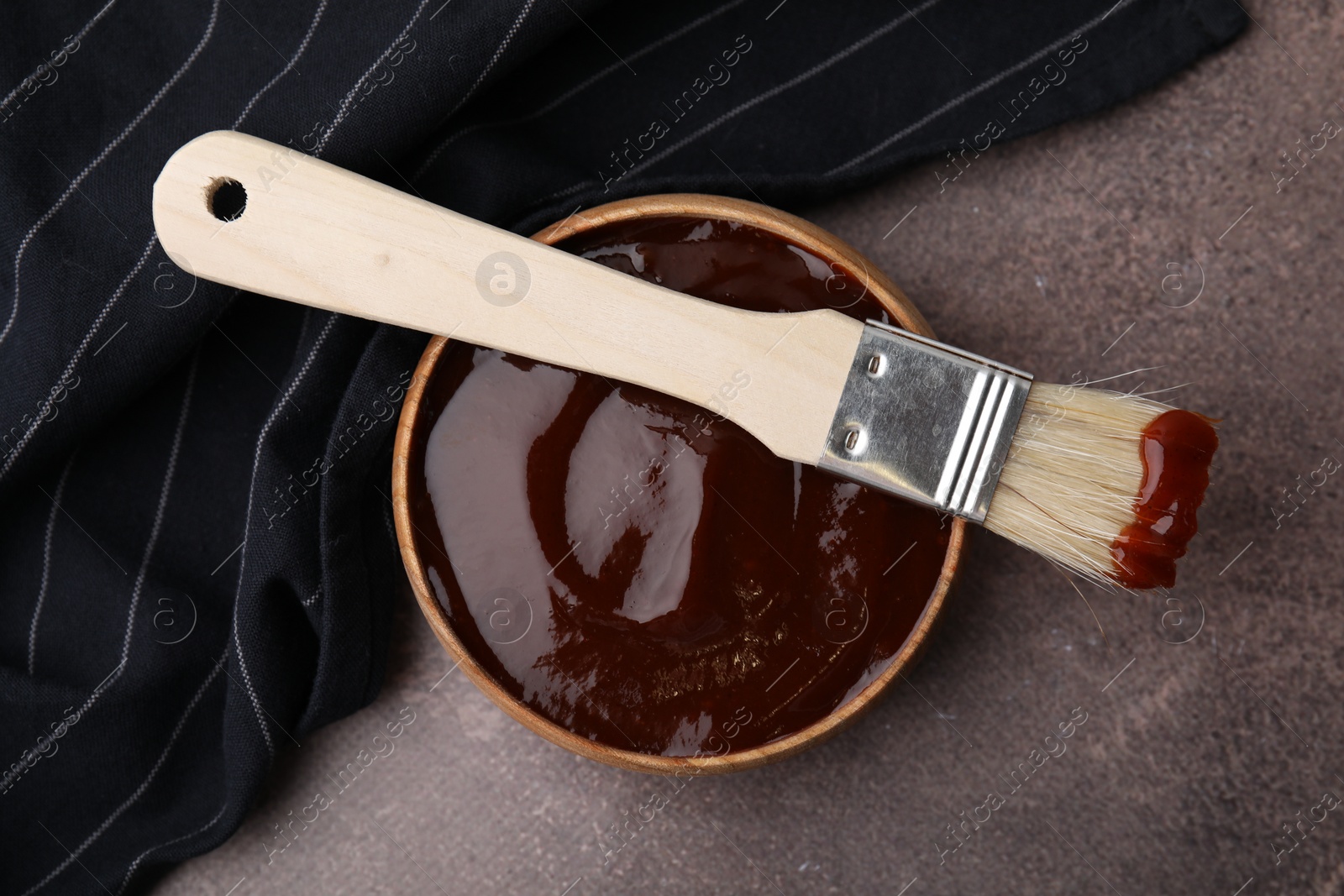 Photo of Marinade in bowl and basting brush on brown table, top view