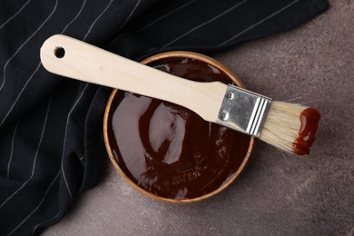 Marinade in bowl and basting brush on brown table, top view