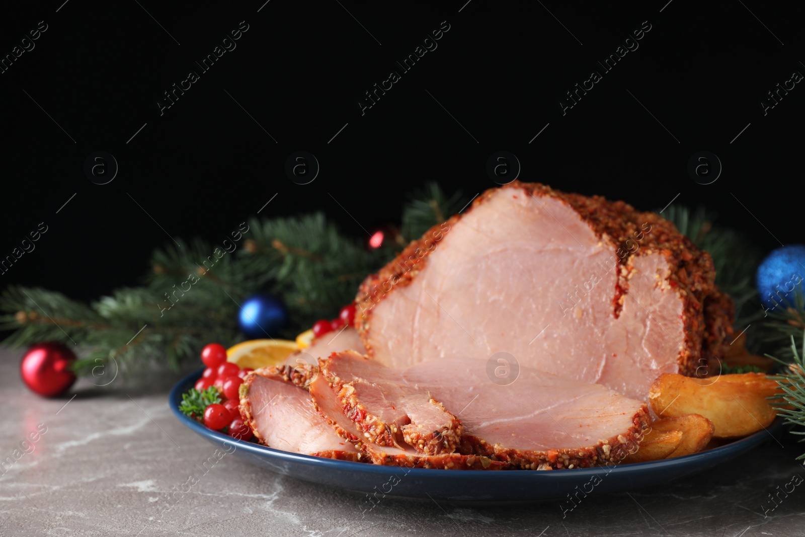 Photo of Plate with Christmas ham on grey table against black background