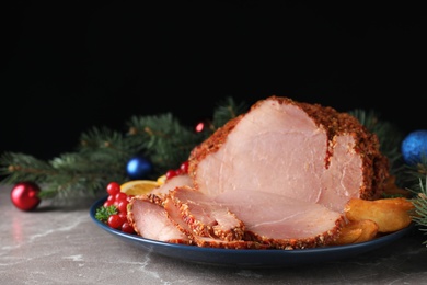 Plate with Christmas ham on grey table against black background