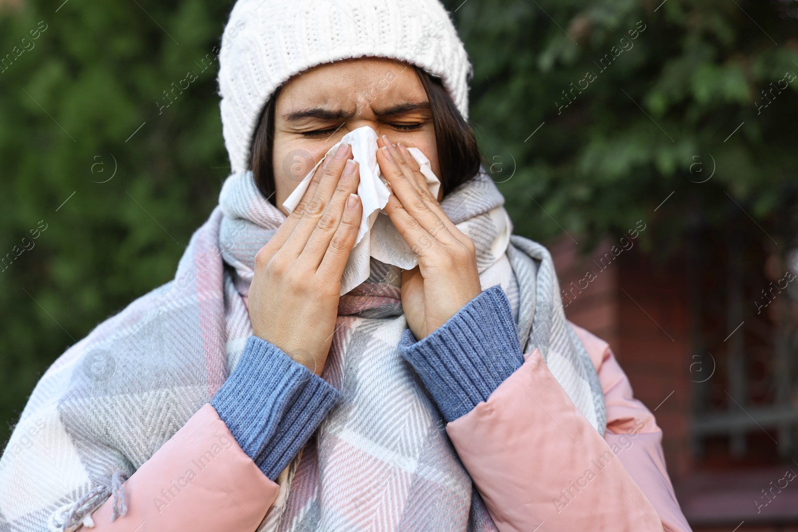 Photo of Woman with tissue blowing runny nose outdoors. Cold symptom