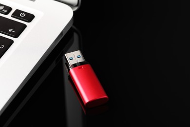 Photo of Modern usb flash drive near laptop on black table