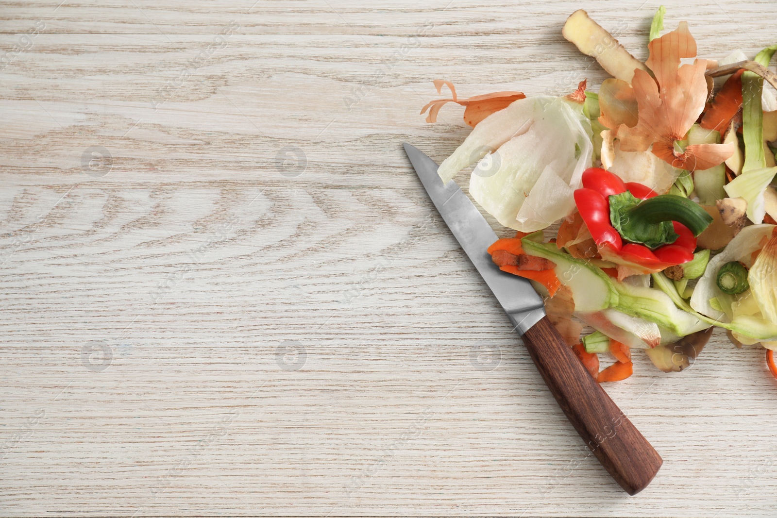 Photo of Peels of fresh vegetables and knife on white wooden table, flat lay. Space for text