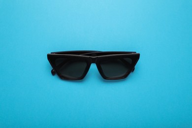 Stylish sunglasses on light blue background, top view