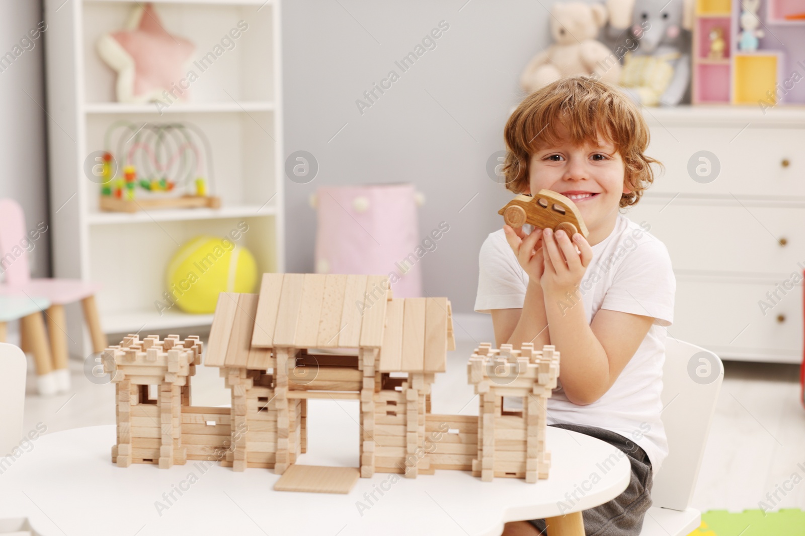 Photo of Little boy playing with wooden entry gate and car at white table in room. Child's toys