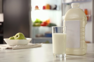 Photo of Gallon and glass of milk on table in kitchen, space for text