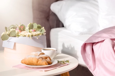 Photo of Plate with delicious croissants and cup of coffee on table near bed