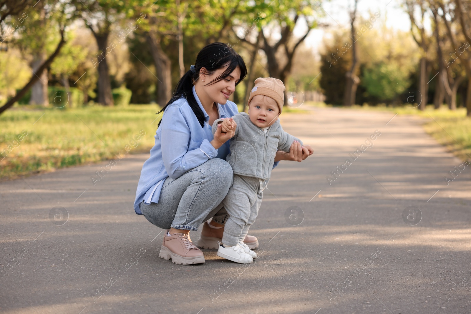 Photo of Mother supporting her baby while he learning to walk outdoors