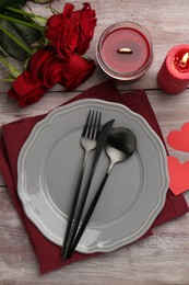 Romantic place setting with red roses, candles and decorative hearts on wooden table, flat lay. St. Valentine's day dinner