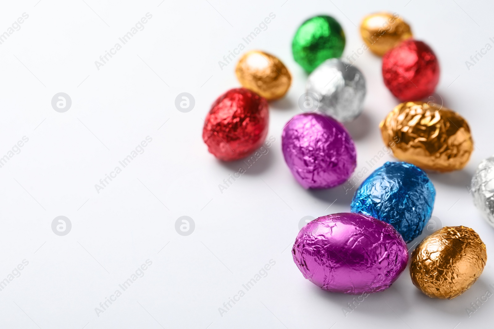 Photo of Chocolate eggs wrapped in colorful foil on white background. Space for text